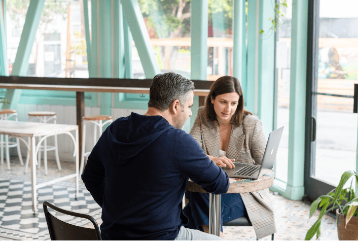 Two employees at a coffee shop sharing a laptop and discussing sales